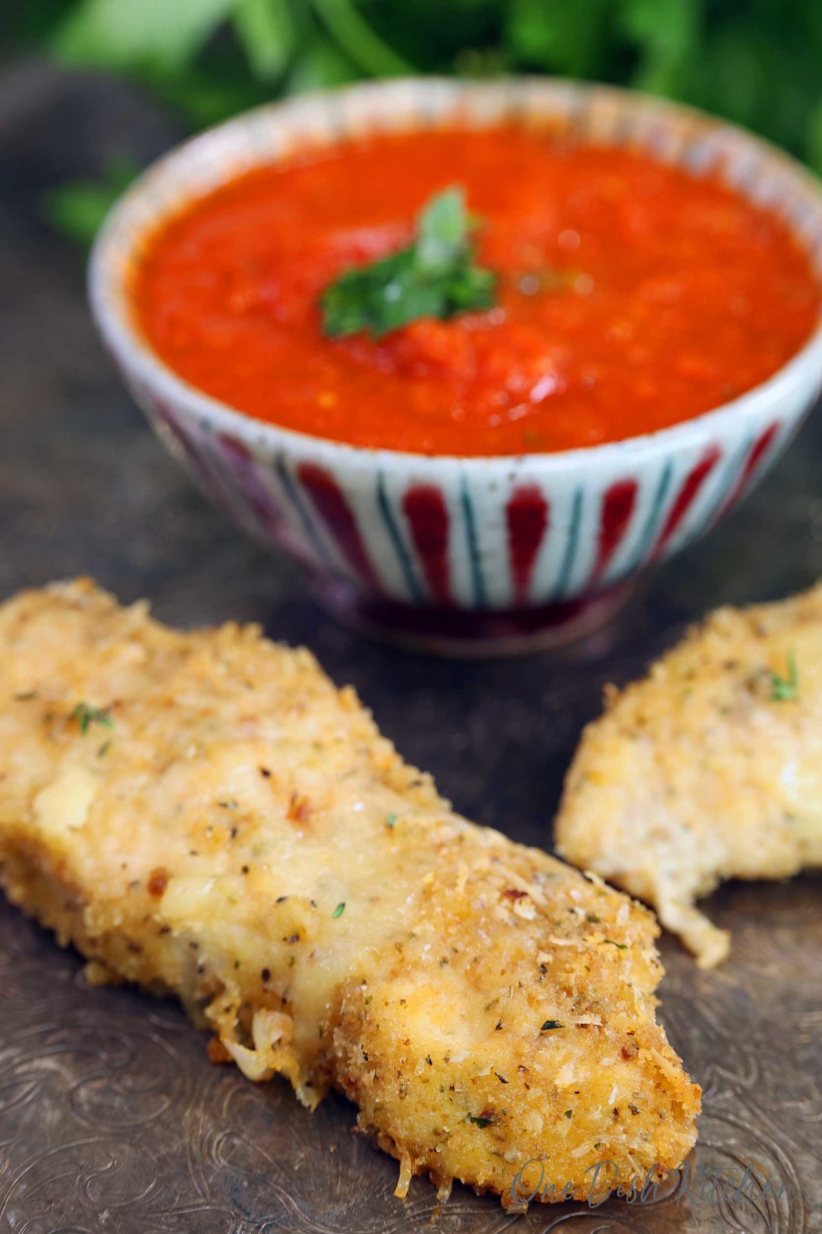 two chicken parmesan tenders on a silver tray next to a bowl of tomato sauce.