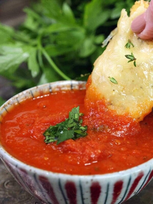 marinara sauce in a small bowl with a chicken tender held by a hand and dipped into the sauce