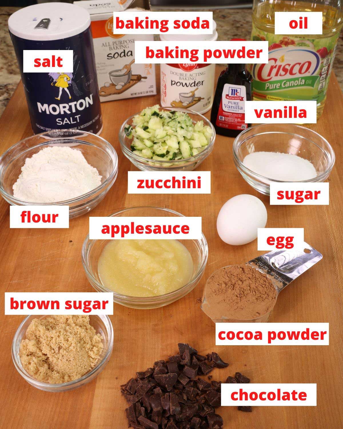 ingredients needed to make chocolate zucchini bread on a wooden cutting board in a kitchen.