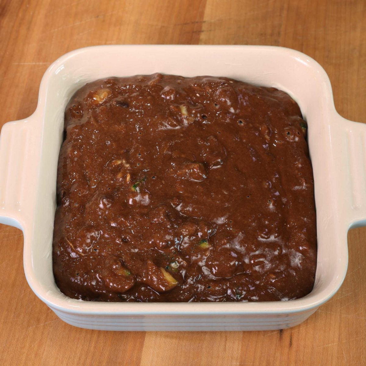 chocolate cake batter in a small blue baking dish on a brown table.