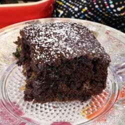 a slice of chocolate zucchini bread on a floral plate next to a red baking dish with the remaining bread inside.