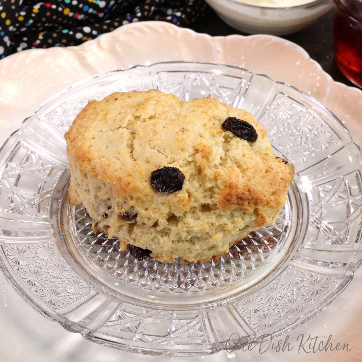 one cream scone with raisins on a clear plate.