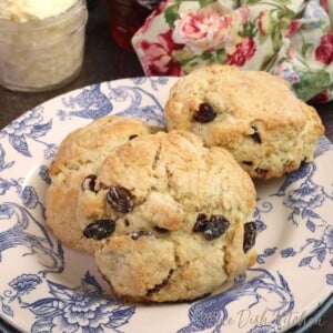 three raisin filled scones on a blue and white plate next to a floral napkin