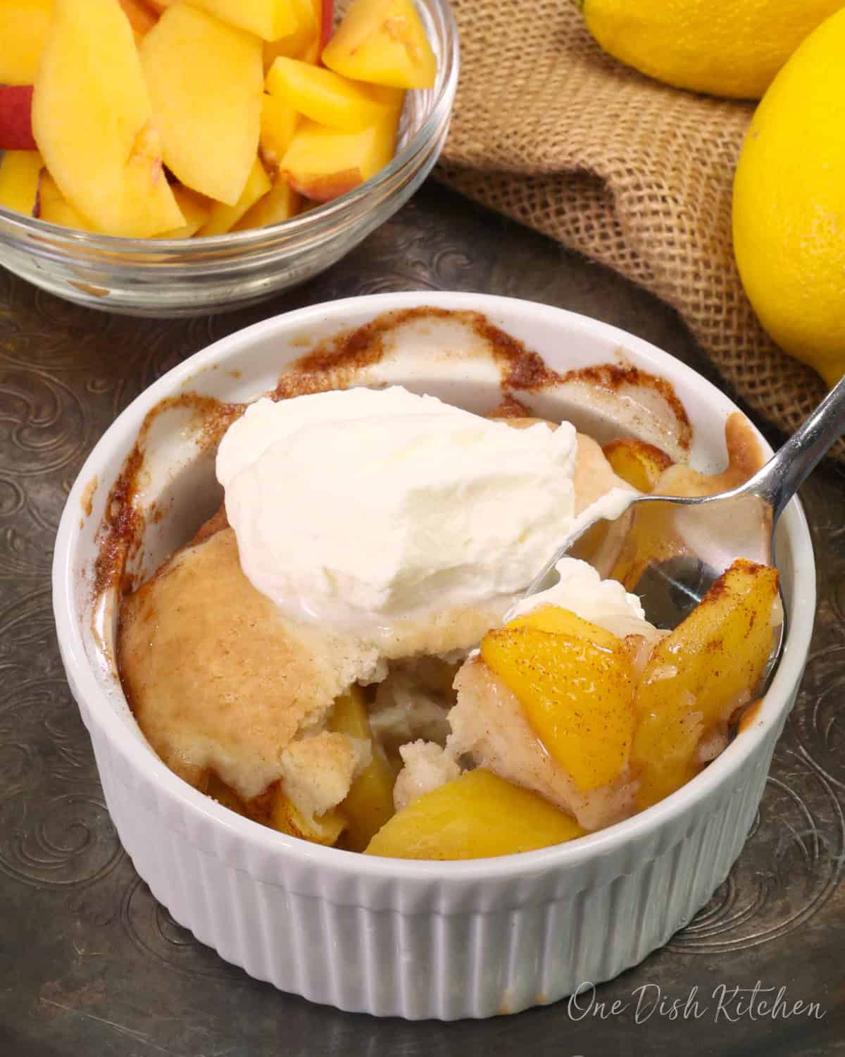 a spoonful of peaches from a peach cobbler with the cobbler in the background.