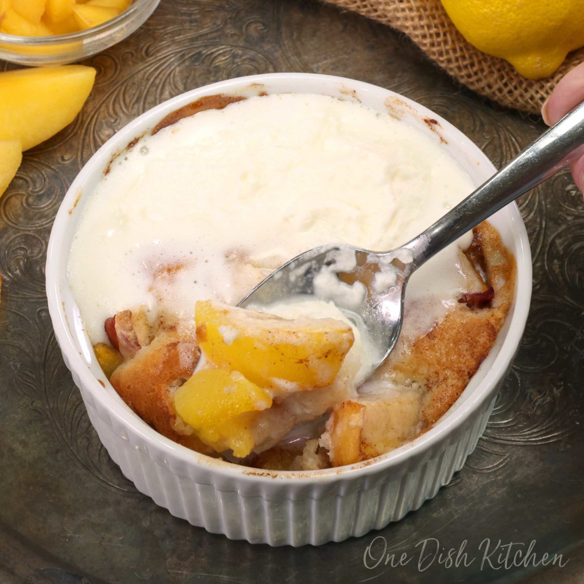 a spoon in the corner of a bowl of peach cobbler with peaches and whipped cream on the spoon.