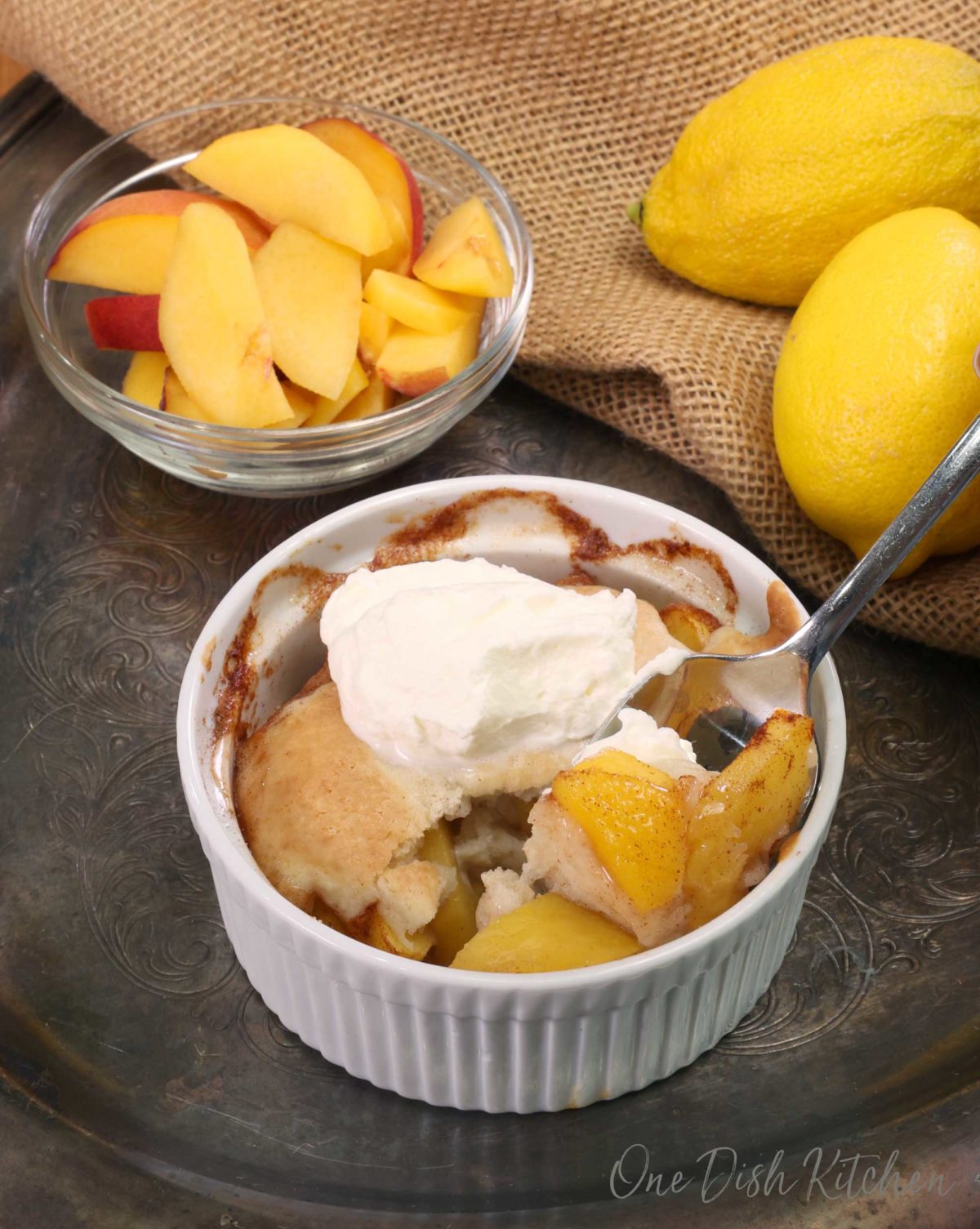 a spoonful of peaches from a peach cobbler with the cobbler in the background.