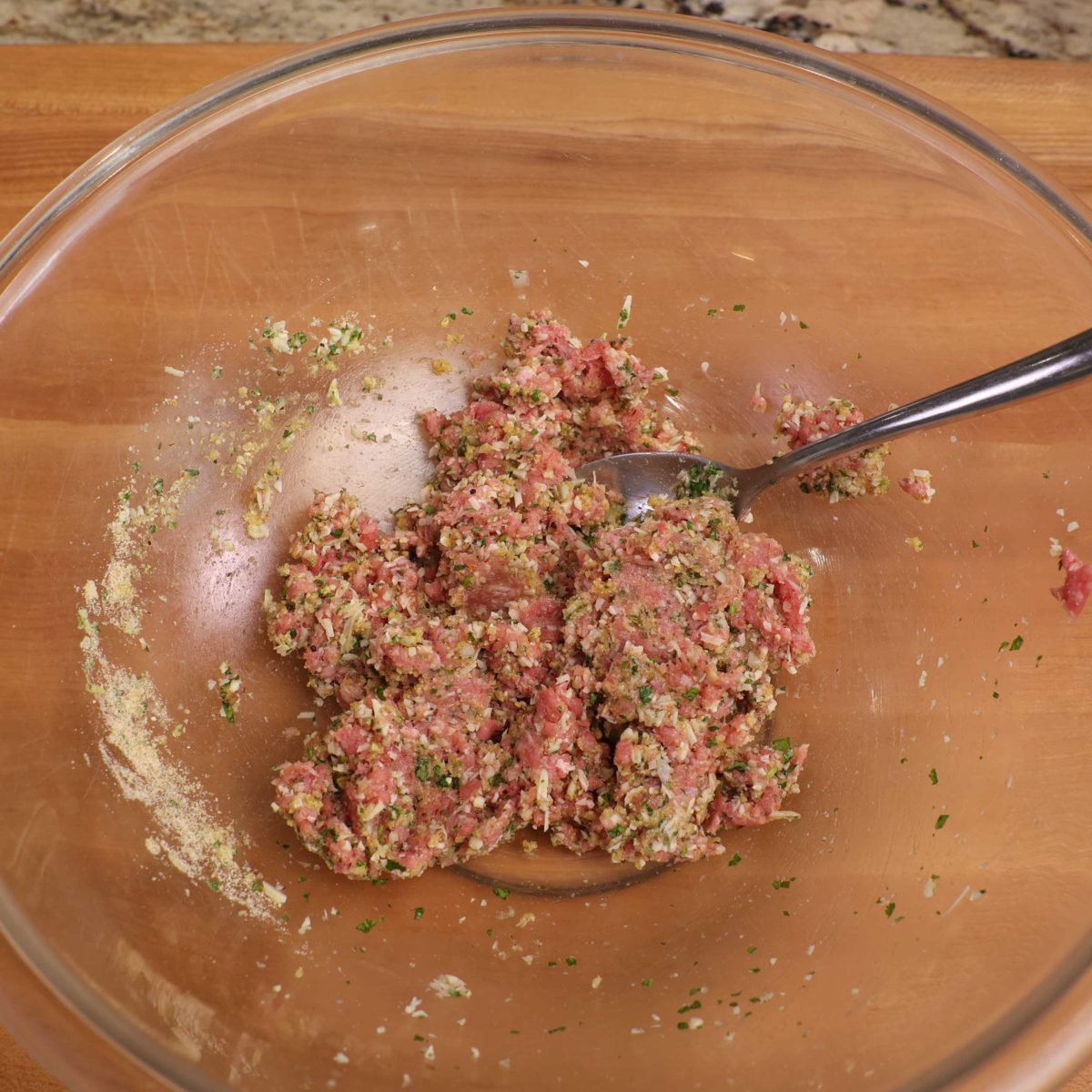 ground beef and other ingredients in meatballs in a large clear mixing bowl.