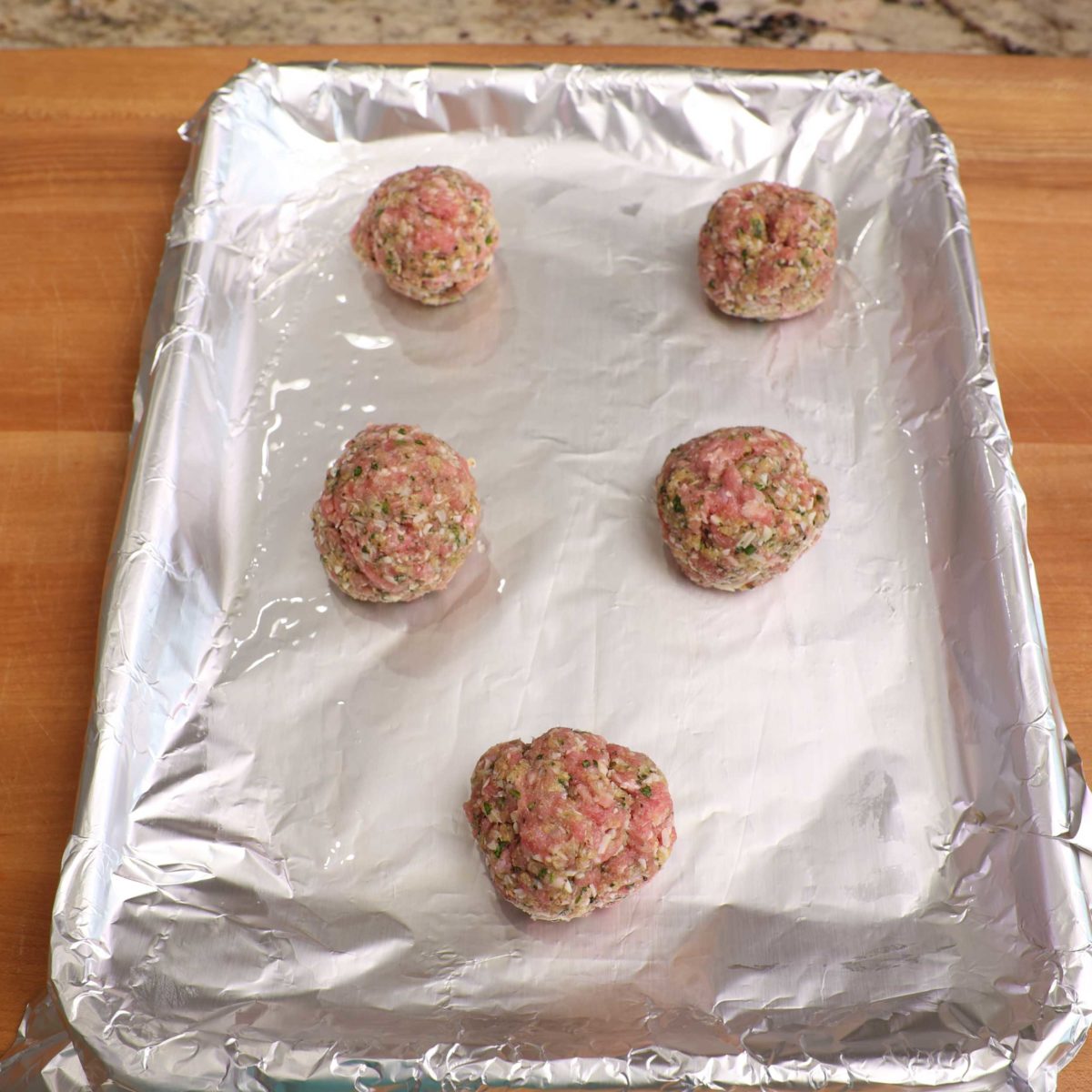 5 meatballs on a baking sheet.