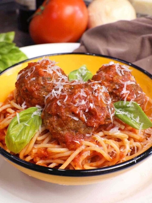 a bowl of spaghetti topped with three meatballs and fresh basil on a white plate next to a bottle of red wine