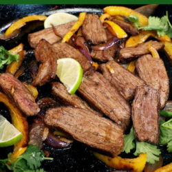 beef fajita meat in a black cast iron skillet topped with cilantro and lime slices