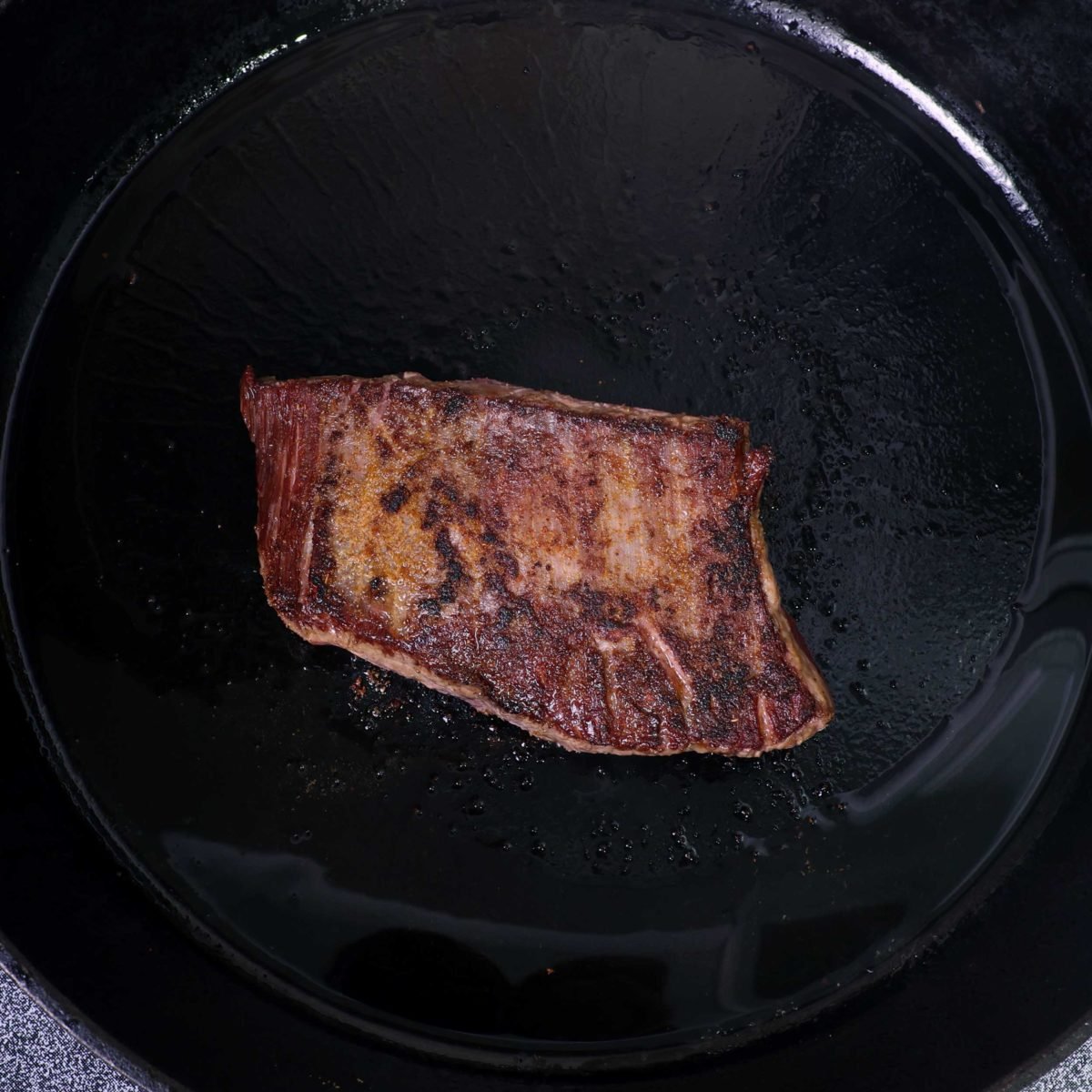 a small piece of steak cooking in a cast iron skillet.