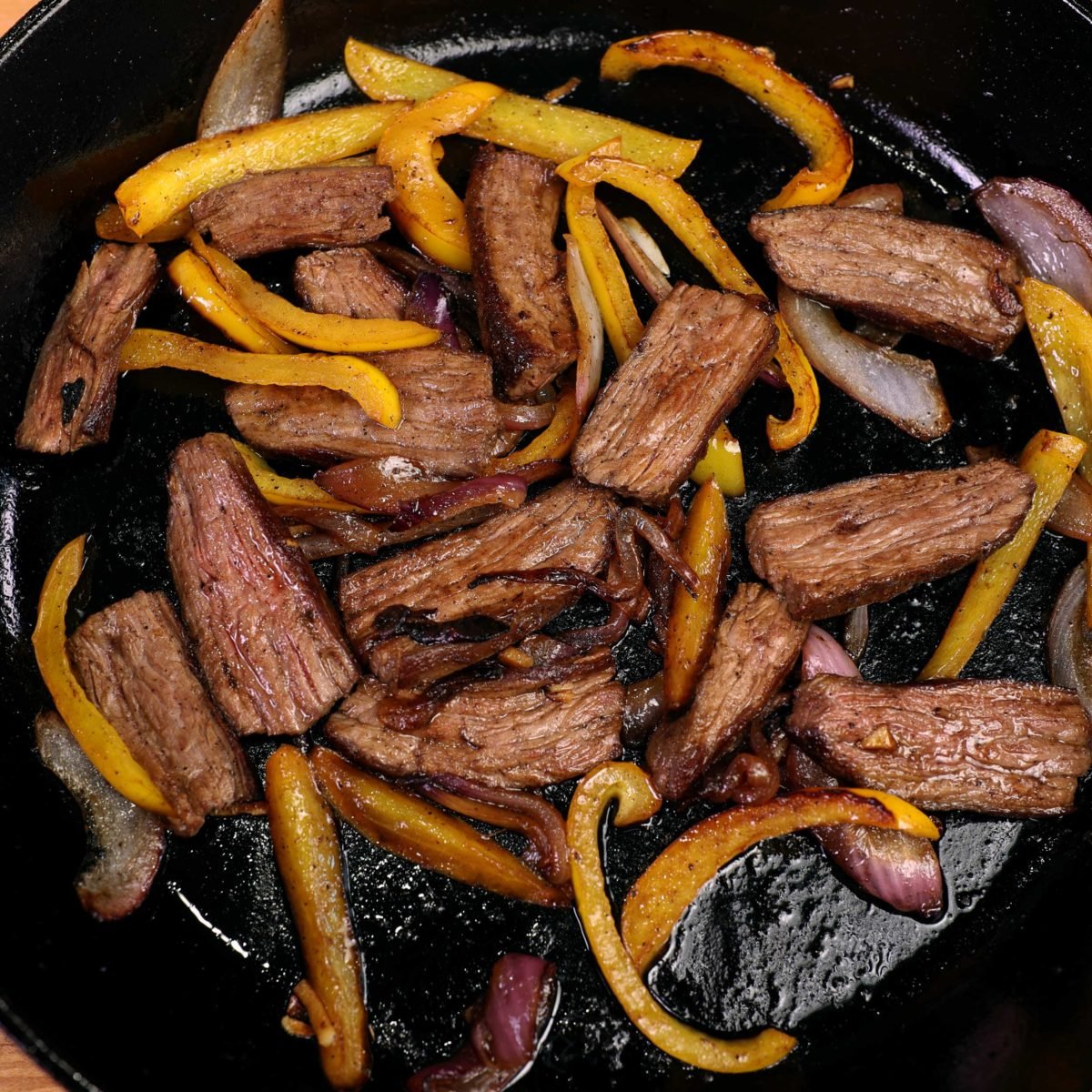 slices of steak, yellow peppers, and onions in a cast iron skillet.