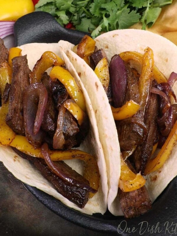 two steak fajitas filled with beef and yellow peppers in a black cast iron plate