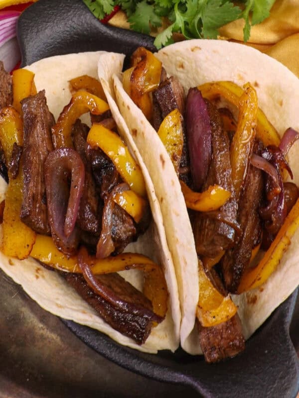 two steak fajitas on a plate surrounded by fresh vegetables.