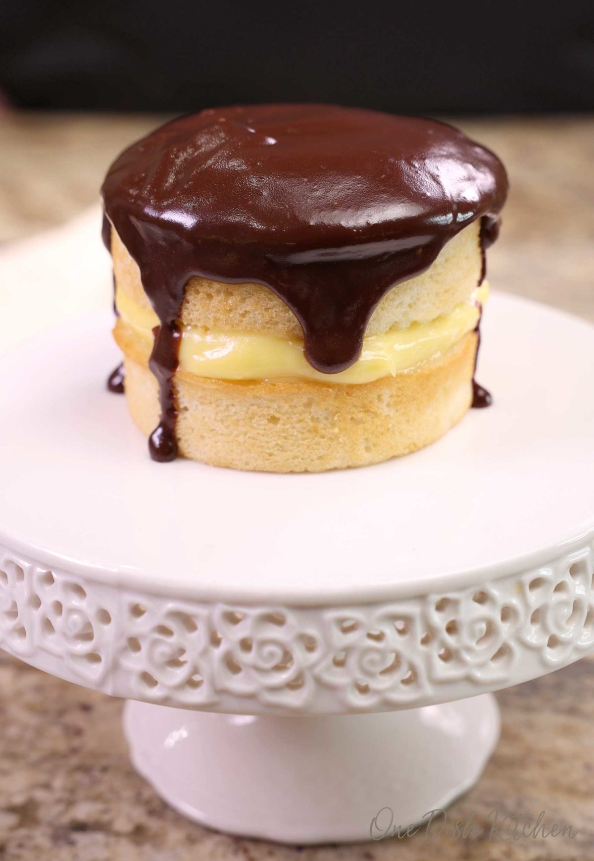 a mini boston cream pie on a white cake stand.