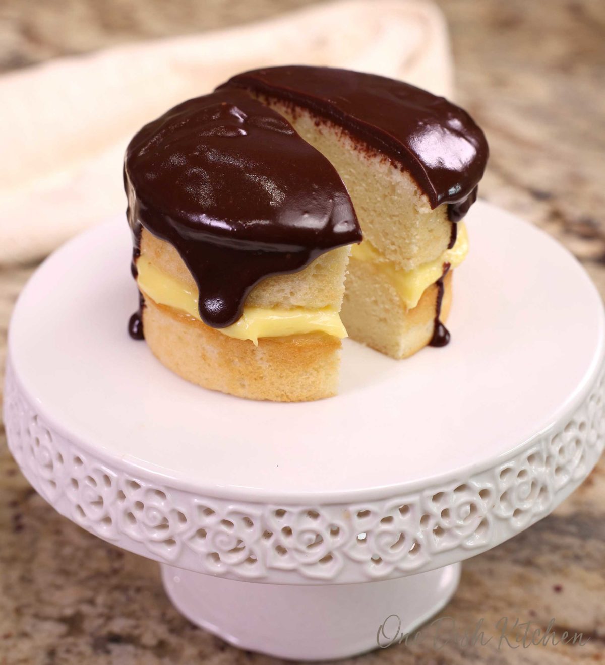 a boston cream pie on a cake stand. The cake is cut in half..