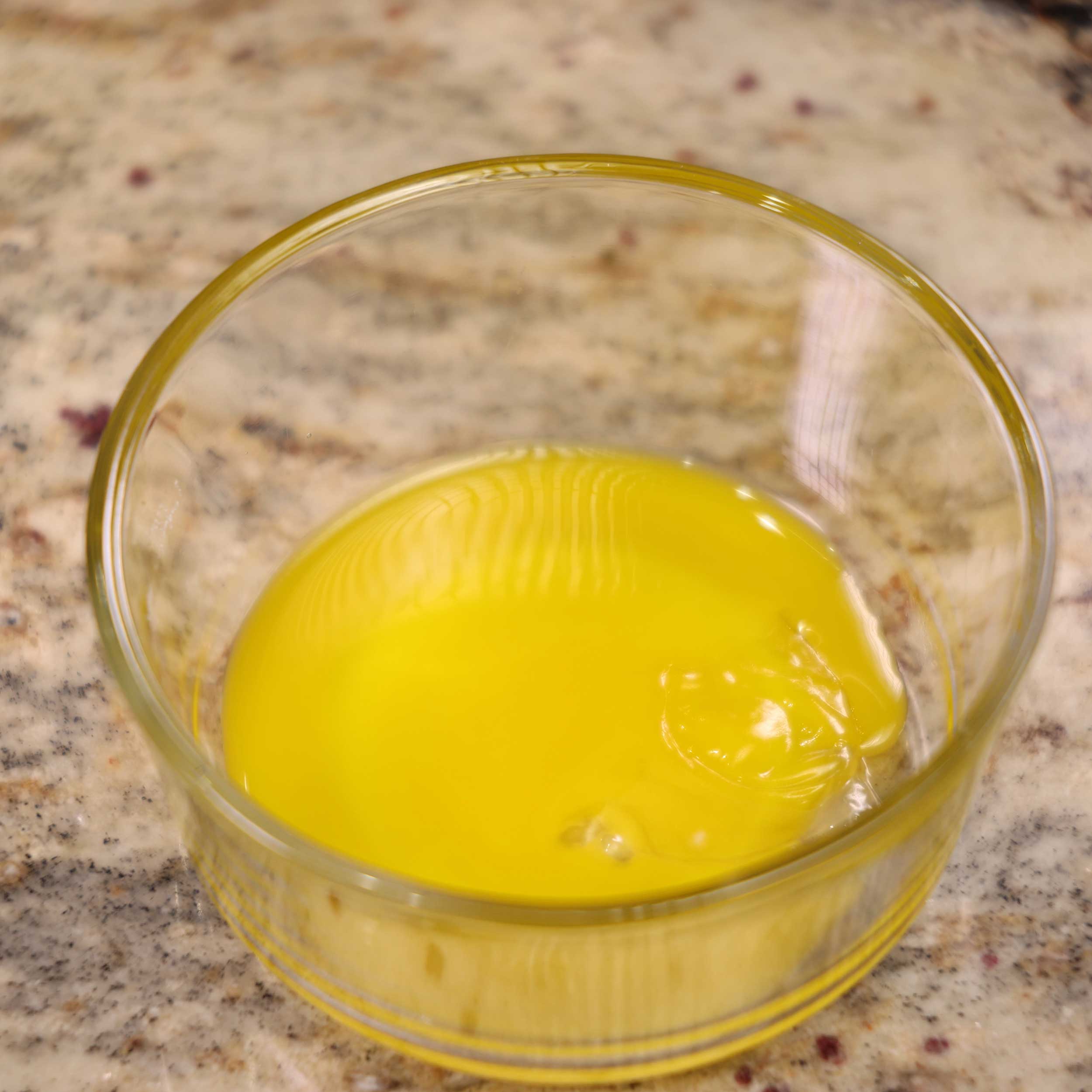 one egg yolk in a clear bowl on a granite counter.