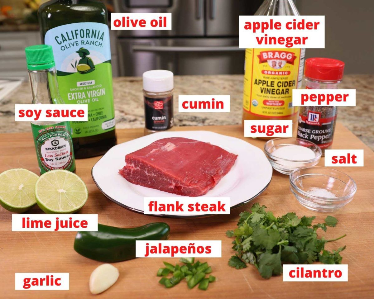 flank steak and all of the ingredients needed to make a carne asada marinade on a wooden cutting board.