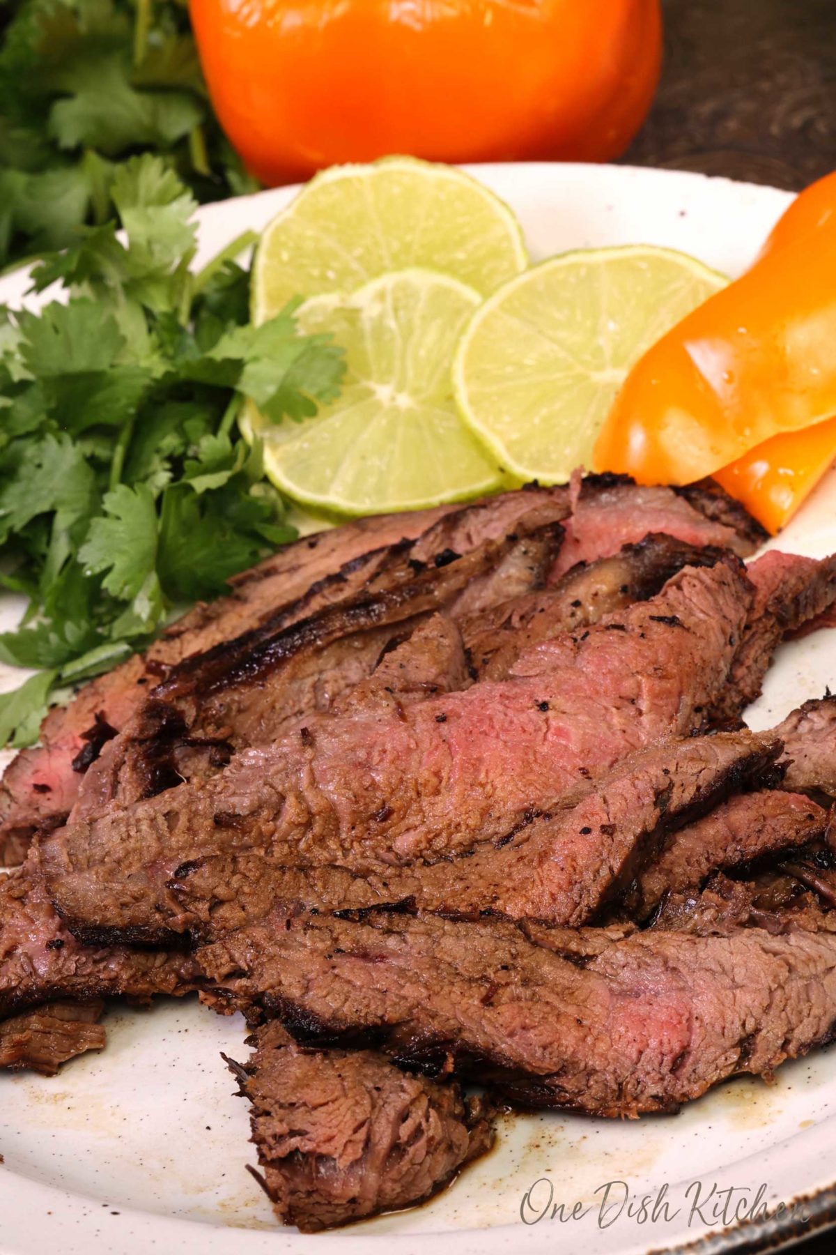 carne asada on a white plate next to vegetables and tortillas.