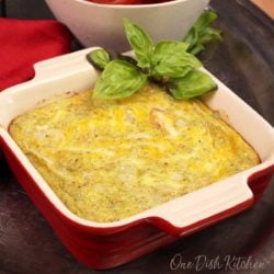 a mini crustless quiche in a red baking dish next to a bowl of tomatoes.