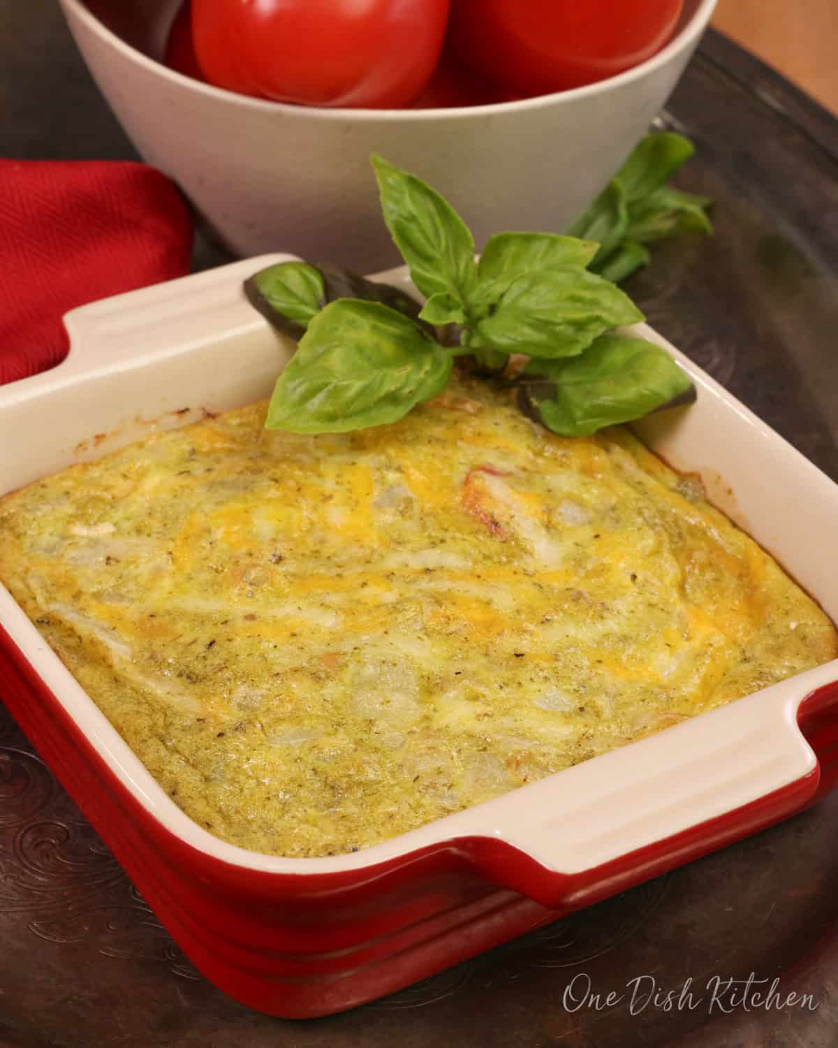 a small crustless tomato quiche with pesto in a small baking dish with fresh basil.