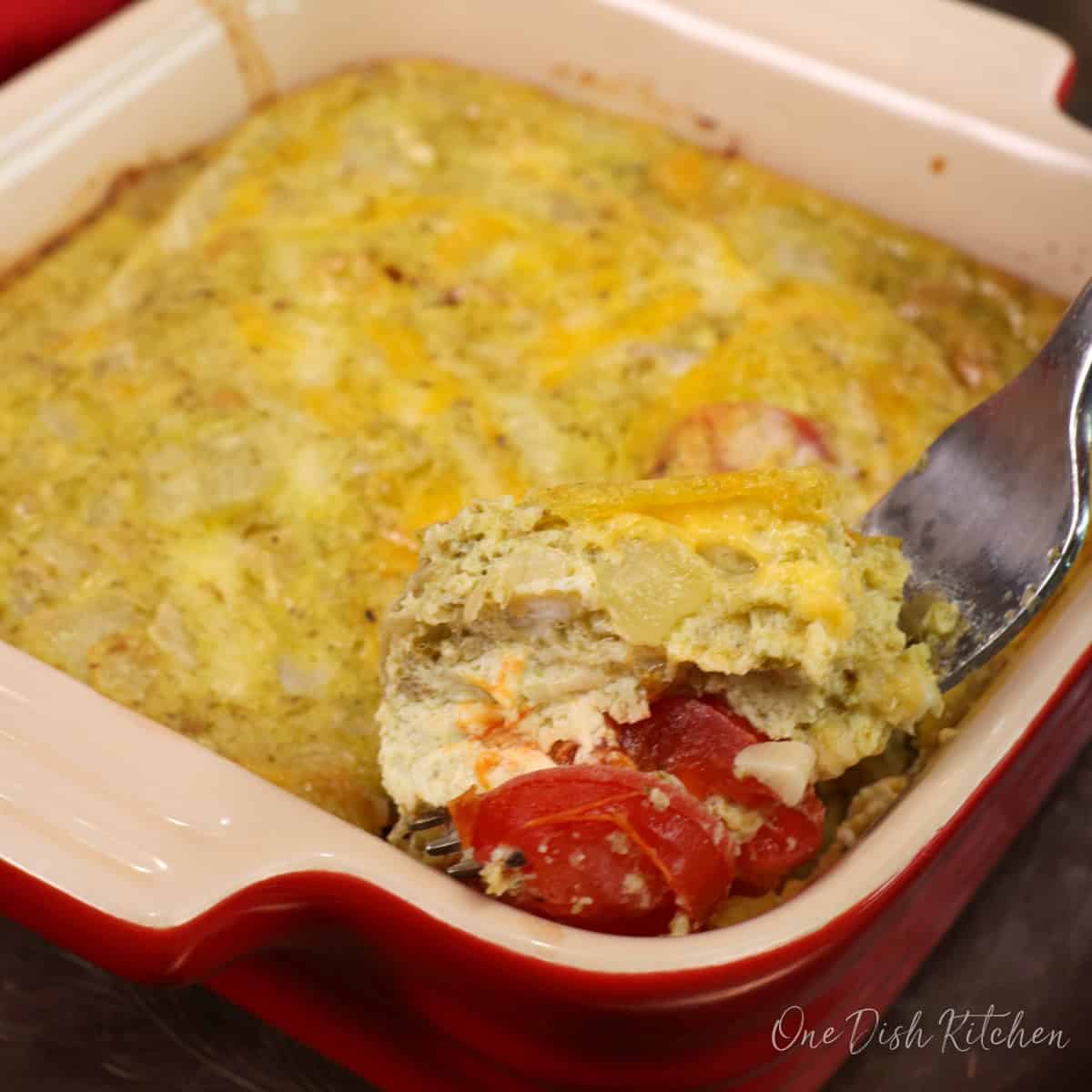 a small crustless tomato quiche with pesto in a red baking dish with a fork on the side.
