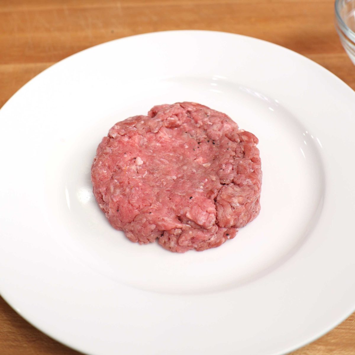 an uncooked hamburger patty on a white plate.