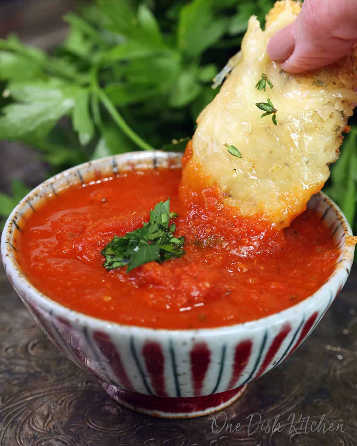 A single parmesan chicken tender dipped in marinara sauce.