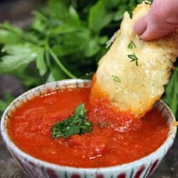 A single parmesan chicken tender dipped in marinara sauce.