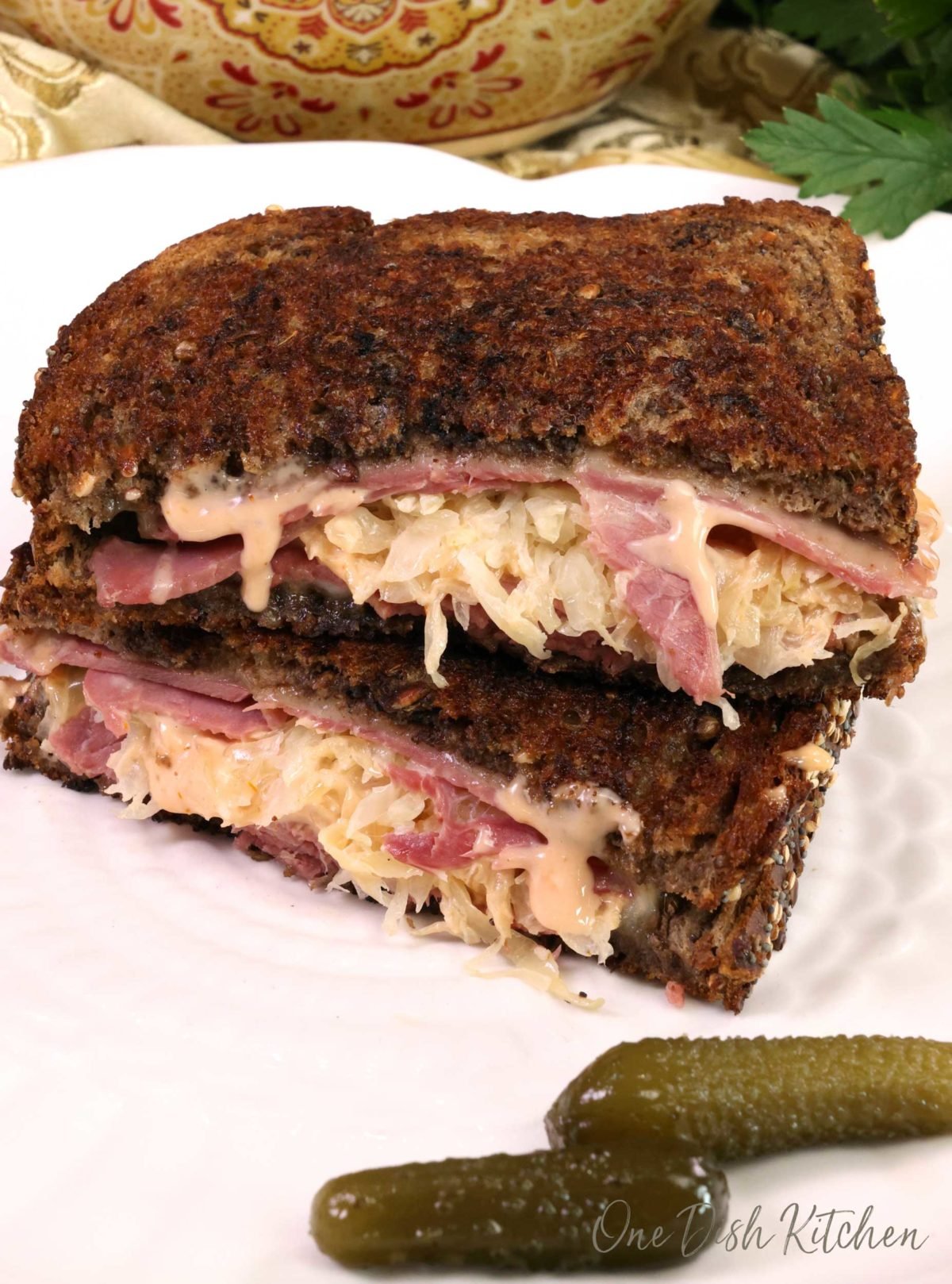 a reuben sandwich on a white plate with two pickles on the side of the plate
