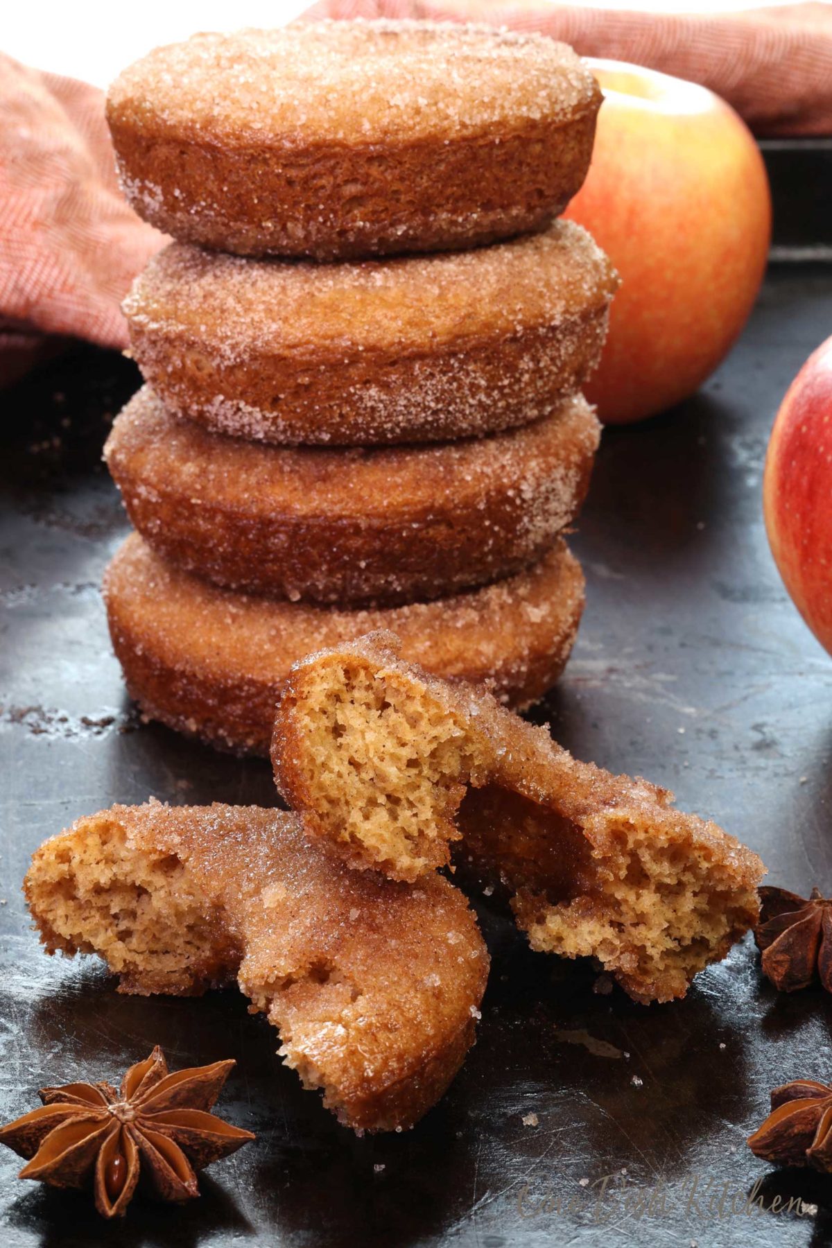 A stack of apple cider donuts on a baking sheet next to one donut cut in half.