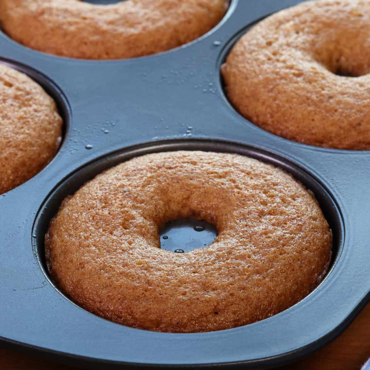 six baked apple cider donuts in a donut pan.