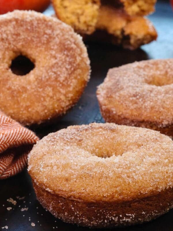 four apple cider donuts with a dusting of cinnamon sugar next to two apples and a star anise.
