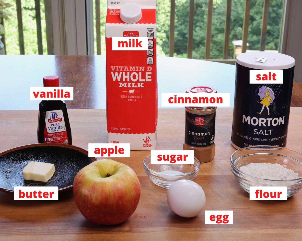 butter, milk, an apple, egg, vanilla, cinnamon, flour and sugar on a wooden cutting board in a kitchen.