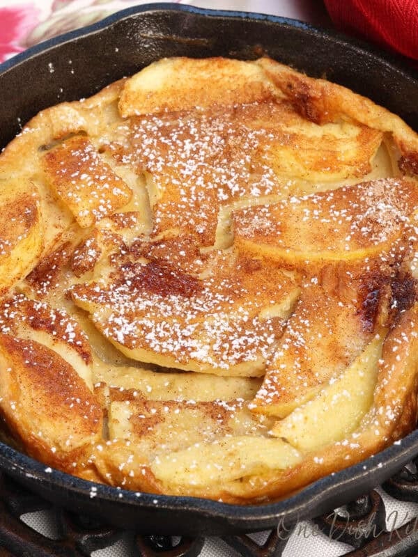 a mini apple dutch baby in a small cast iron skillet next to a red napkin and a bowl of fried apples.