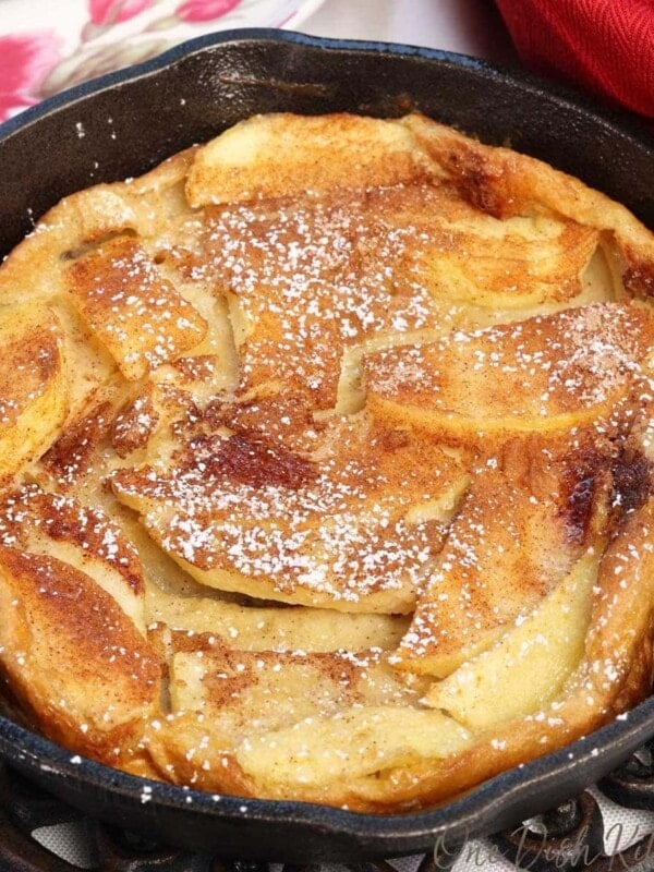a mini apple dutch baby in a small cast iron skillet next to a red napkin and a bowl of fried apples
