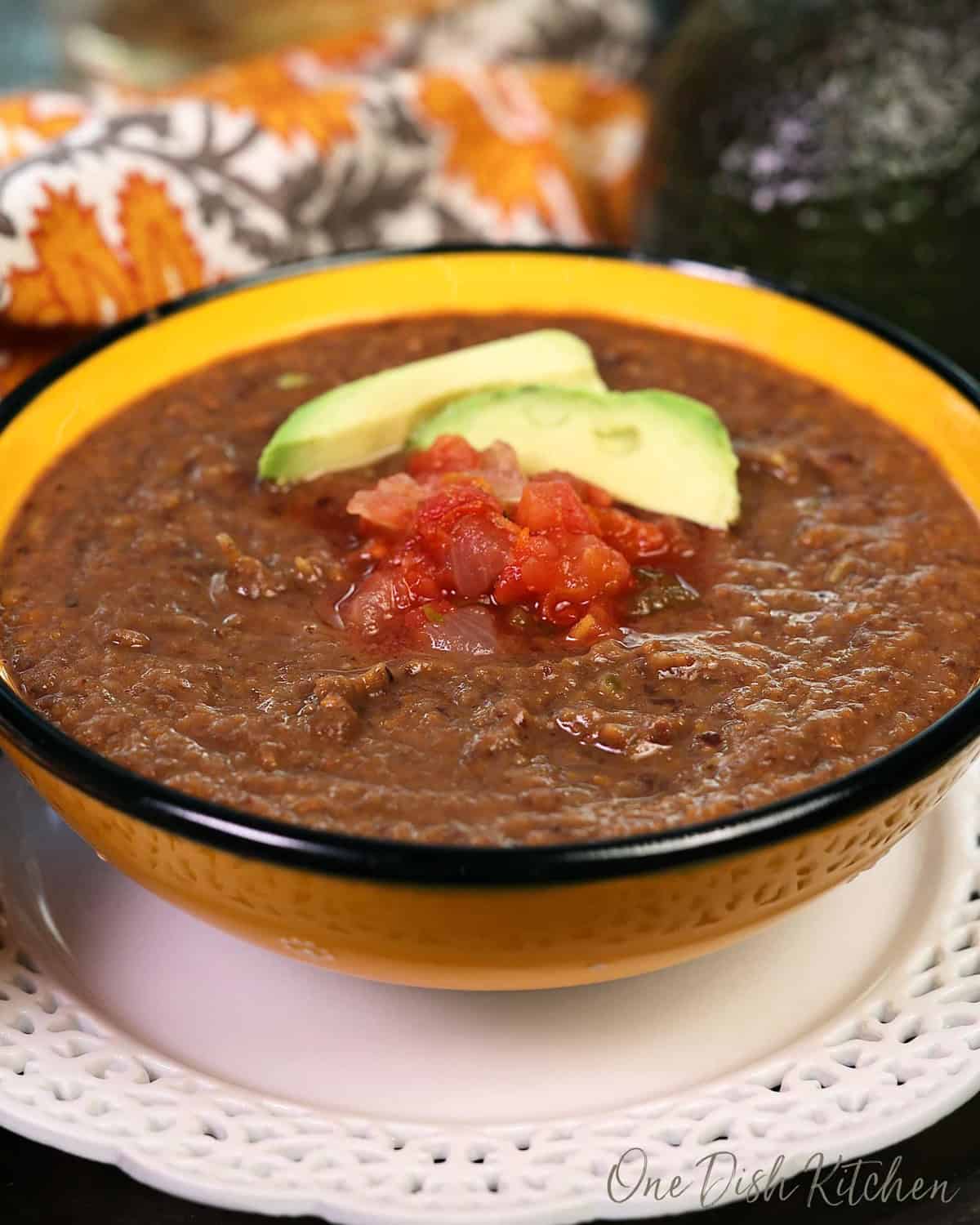 a single serving of black bean soup in a yellow bowl.