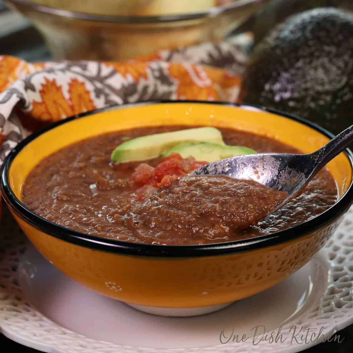 a single serving of canned black bean soup in a bowl topped with salsa and an avocado slice.