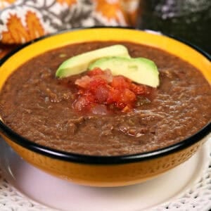 a single serving of canned black bean soup in a bowl topped with salsa and an avocado slice.