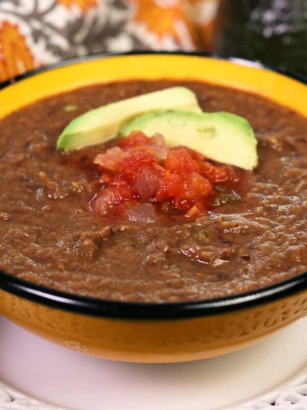 a single serving of canned black bean soup in a bowl topped with salsa and an avocado slice.