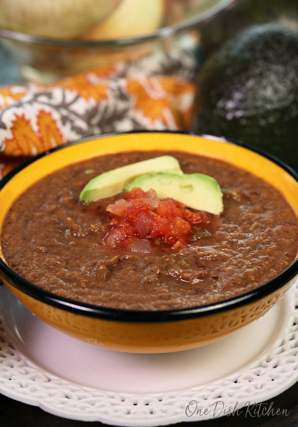 black bean soup in a yellow bowl topped with avocado slices and salsa.
