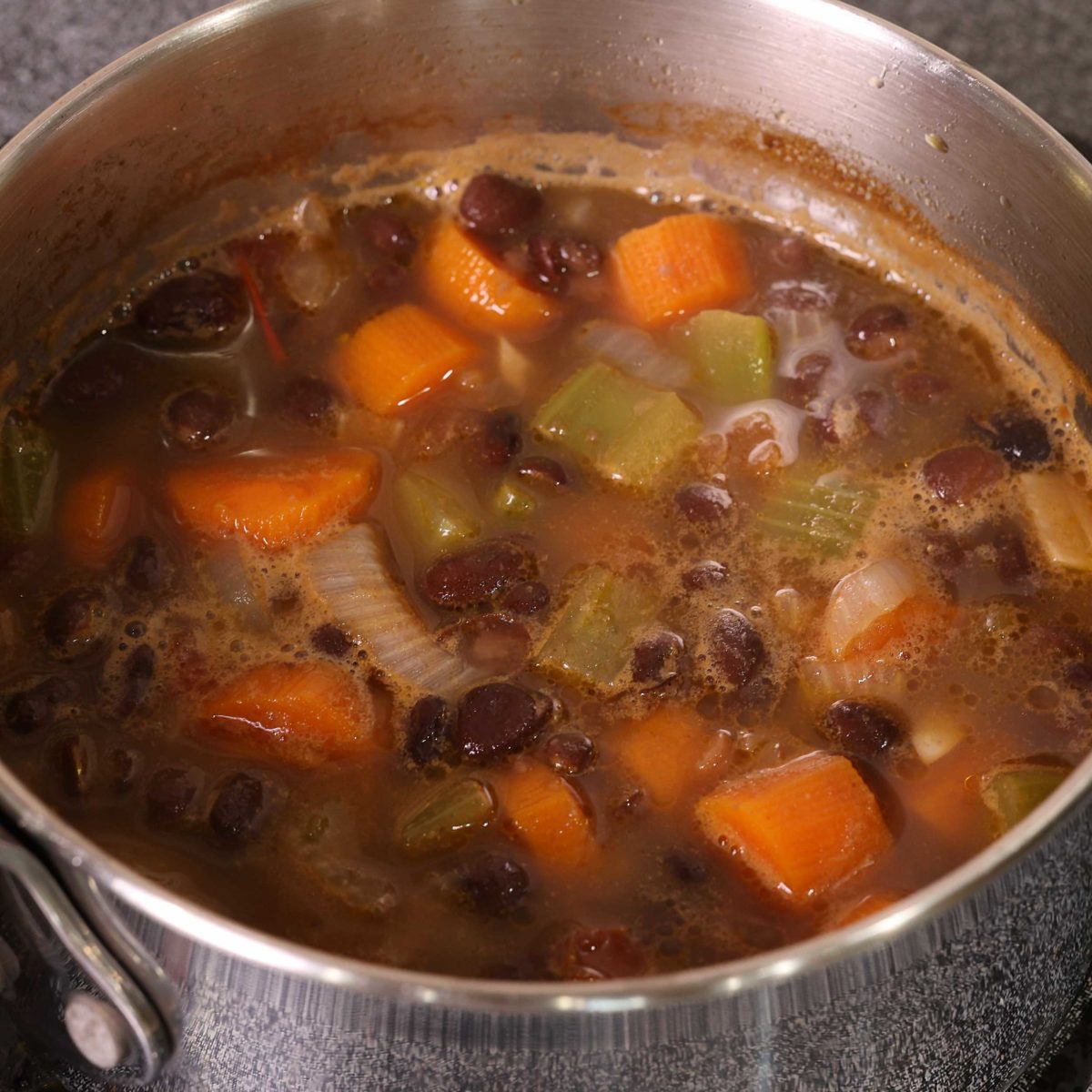 soup simmering on the stove with carrots, black beans, celery, onions, and broth in the pot.