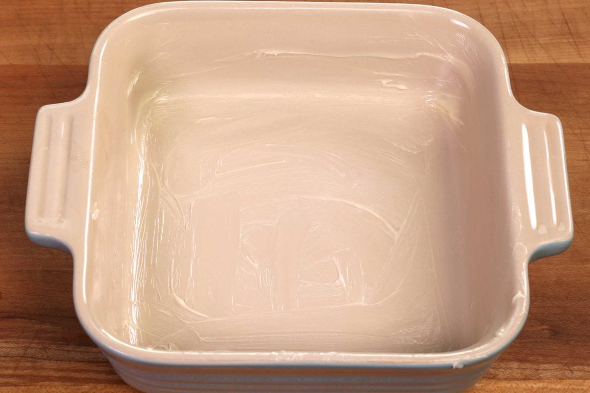 a small square buttered baking dish on a brown table.