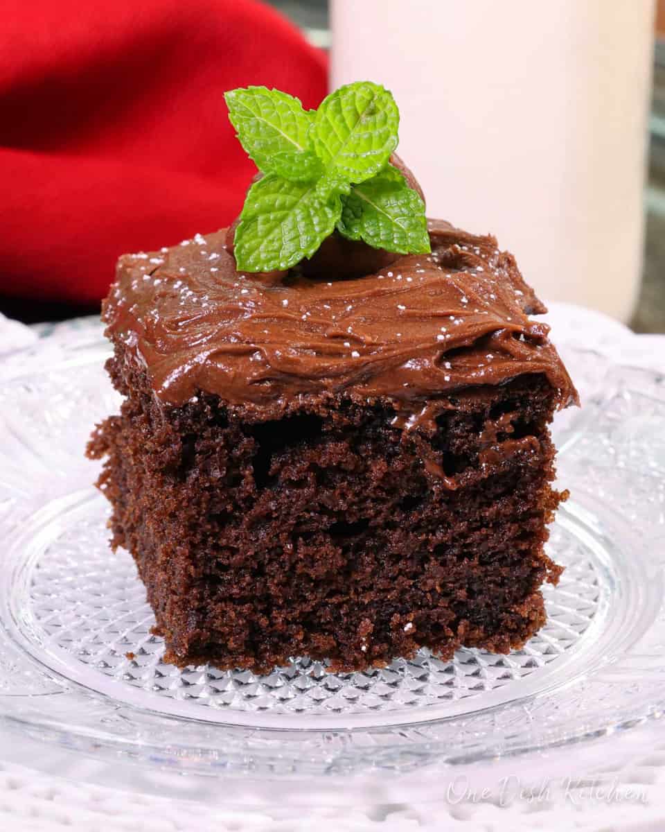 a square piece of devils food cake on a white plate next to a red napkin.