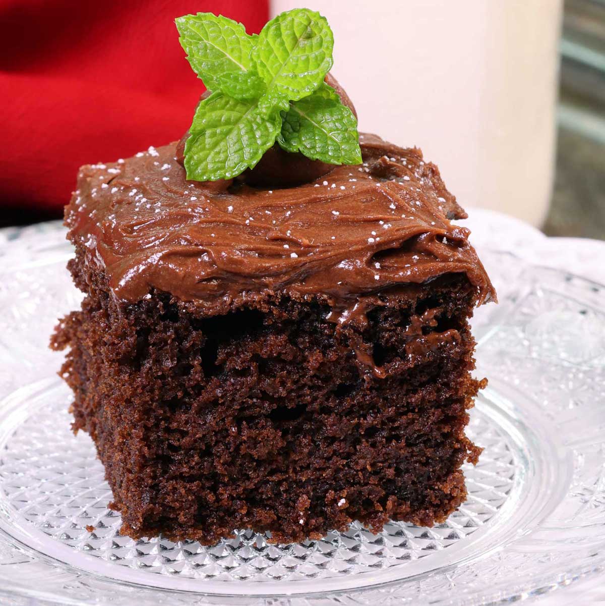 a square piece of devils food cake on a white plate next to a red napkin.