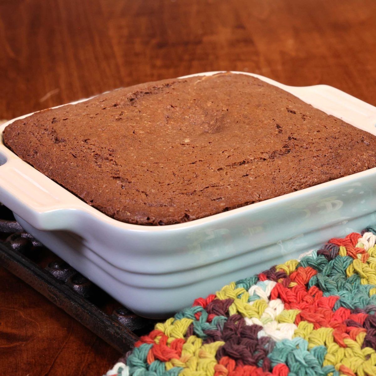 an unfrosted devils food cake in a square baking dish next to a multi-colored napkin.