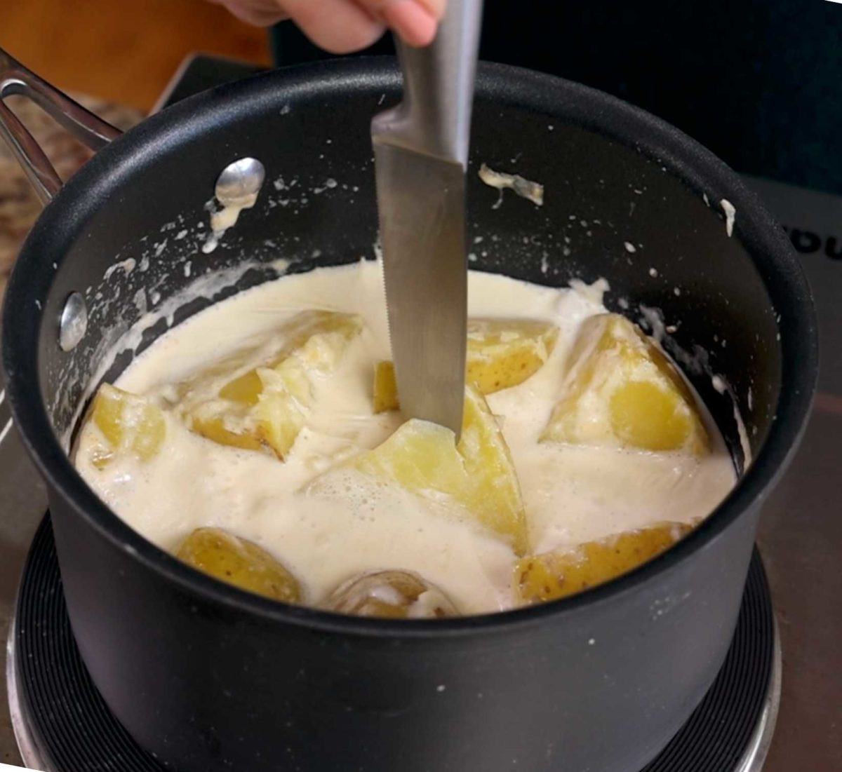 cooked potatoes in a saucepan being pierced with the tip of a knife
