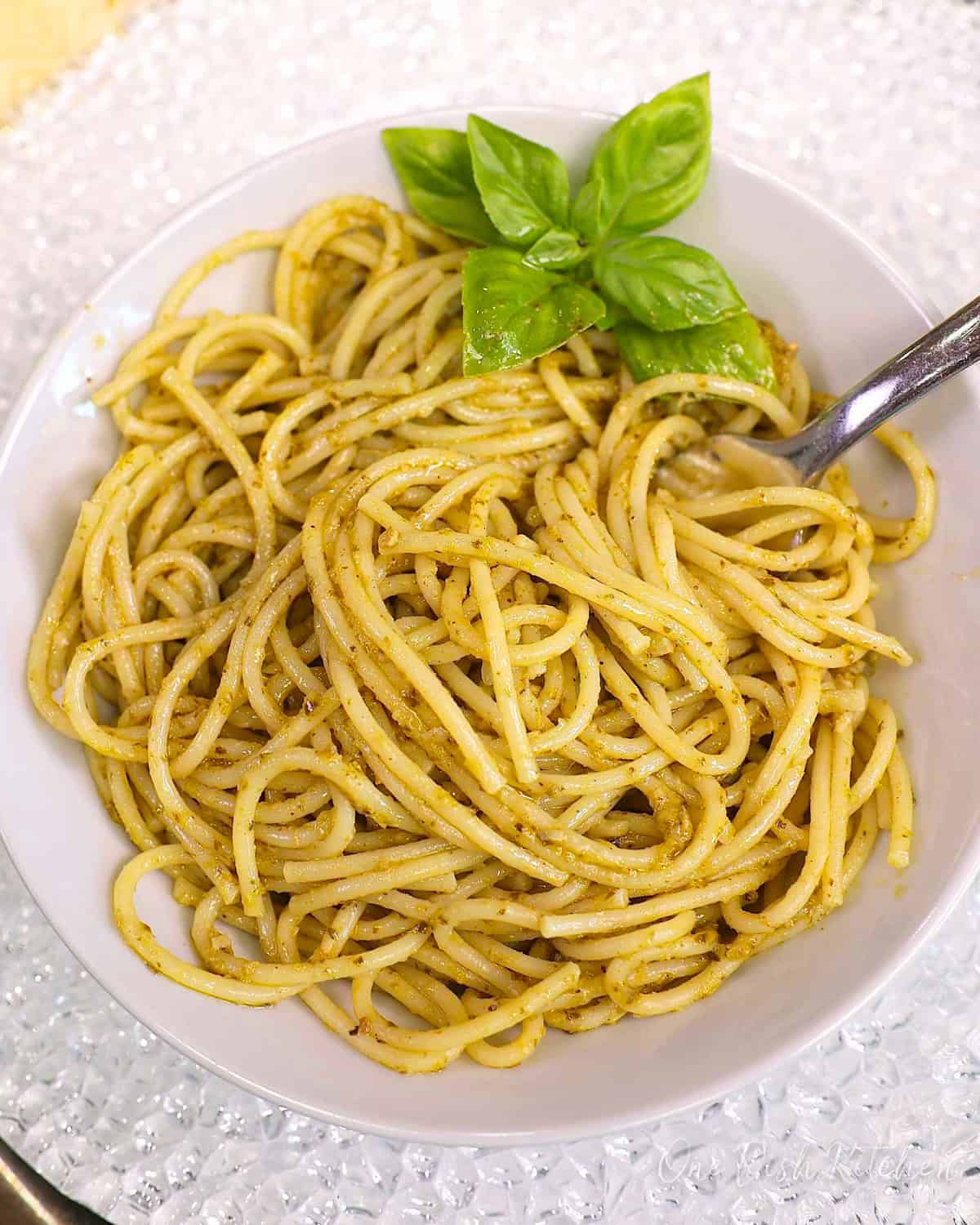 a single serving of pesto pasta in a white bowl with fresh basil on the side.