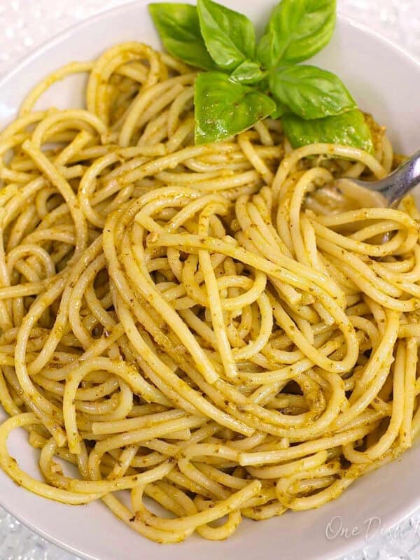 a single serving of pesto pasta in a white bowl with fresh basil on the side.