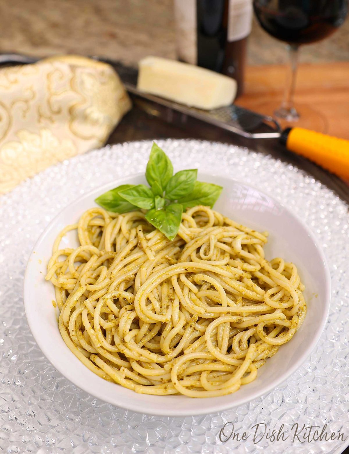 a bowl of pesto pasta with fresh basil on the side next to a bottle of red wine.